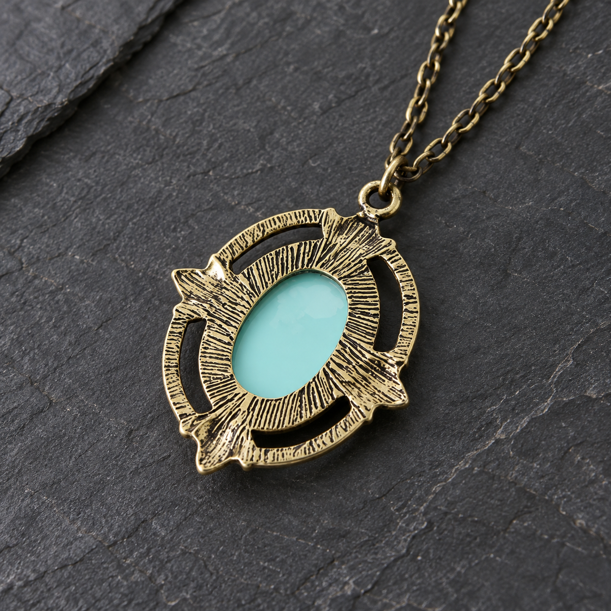 An antique bronze pendant necklace featuring a textured circular frame with an oval light blue turquoise center, displayed on a dark slate background.