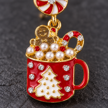A festive Christmas-themed enamel pin shaped like a red mug filled with white pearls, a gingerbread man, a candy cane, and a peppermint candy bar at the top, set against a dark textured background.