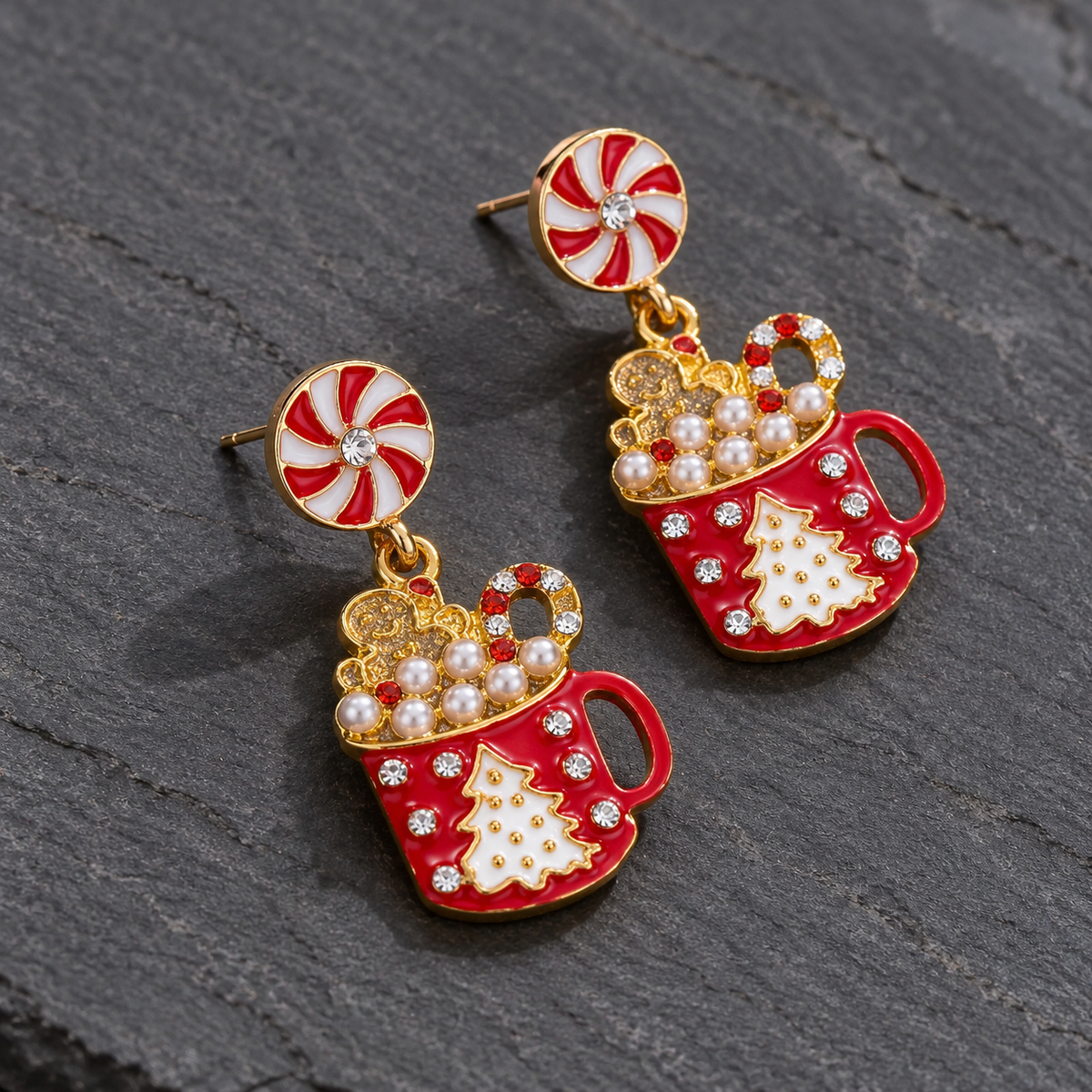 A pair of gold-tone drop earrings with red and white candy cane and Christmas tree mug motifs, accented with faux pearls and rhinestones, displayed on a dark textured slate background.