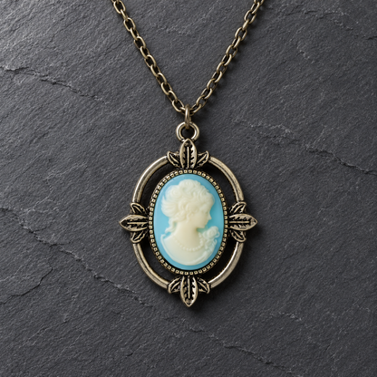 An antique bronze oval pendant necklace featuring a classic cameo-style portrait with a light blue and white background, displayed on a dark slate surface.