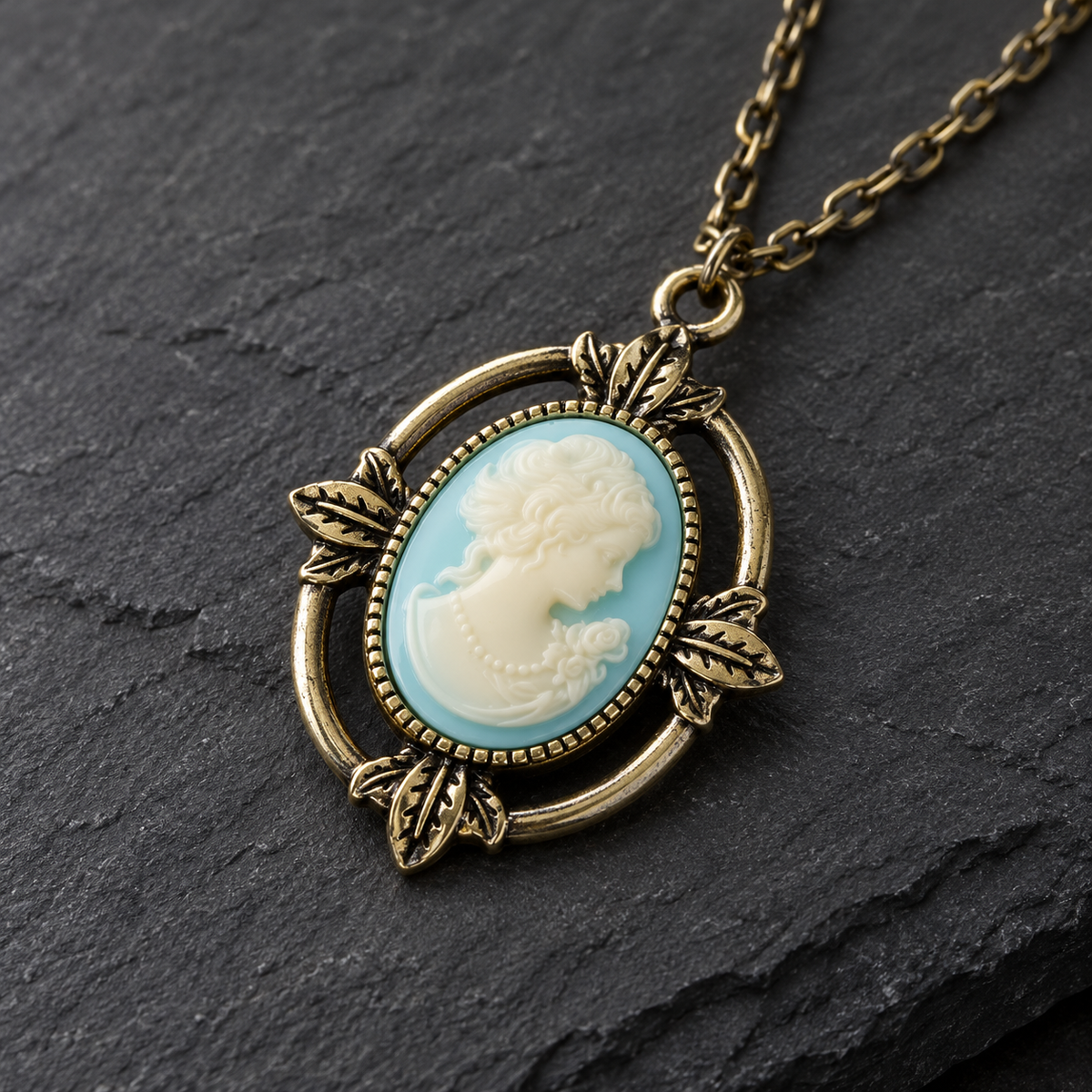 An antique bronze oval pendant necklace featuring a light blue and cream cameo-style profile of a woman, resting on a dark slate surface.