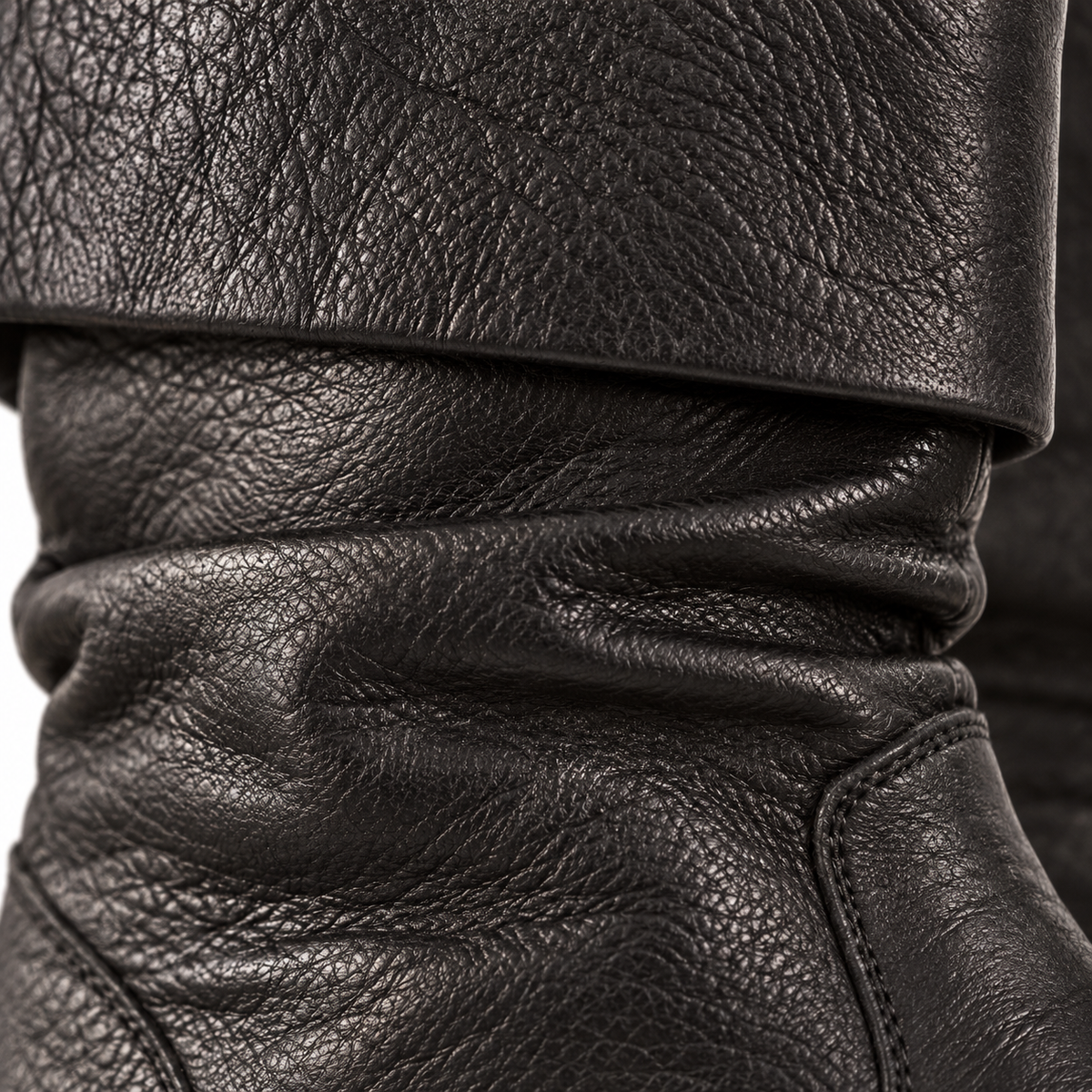 Close-up of a black leather boot showing the pebbled texture, fold-over cuff, and stitched panel details.