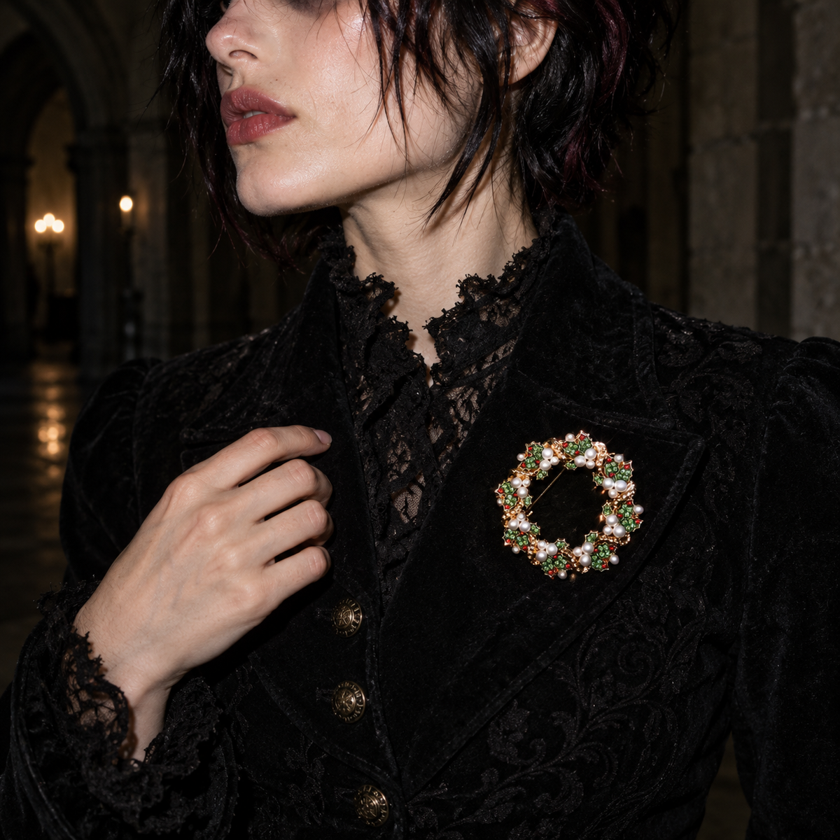A close-up of a woman wearing a black lace and velvet jacket with a decorative circular brooch featuring multicolored rhinestones on the chest, set against a dark, atmospheric background.