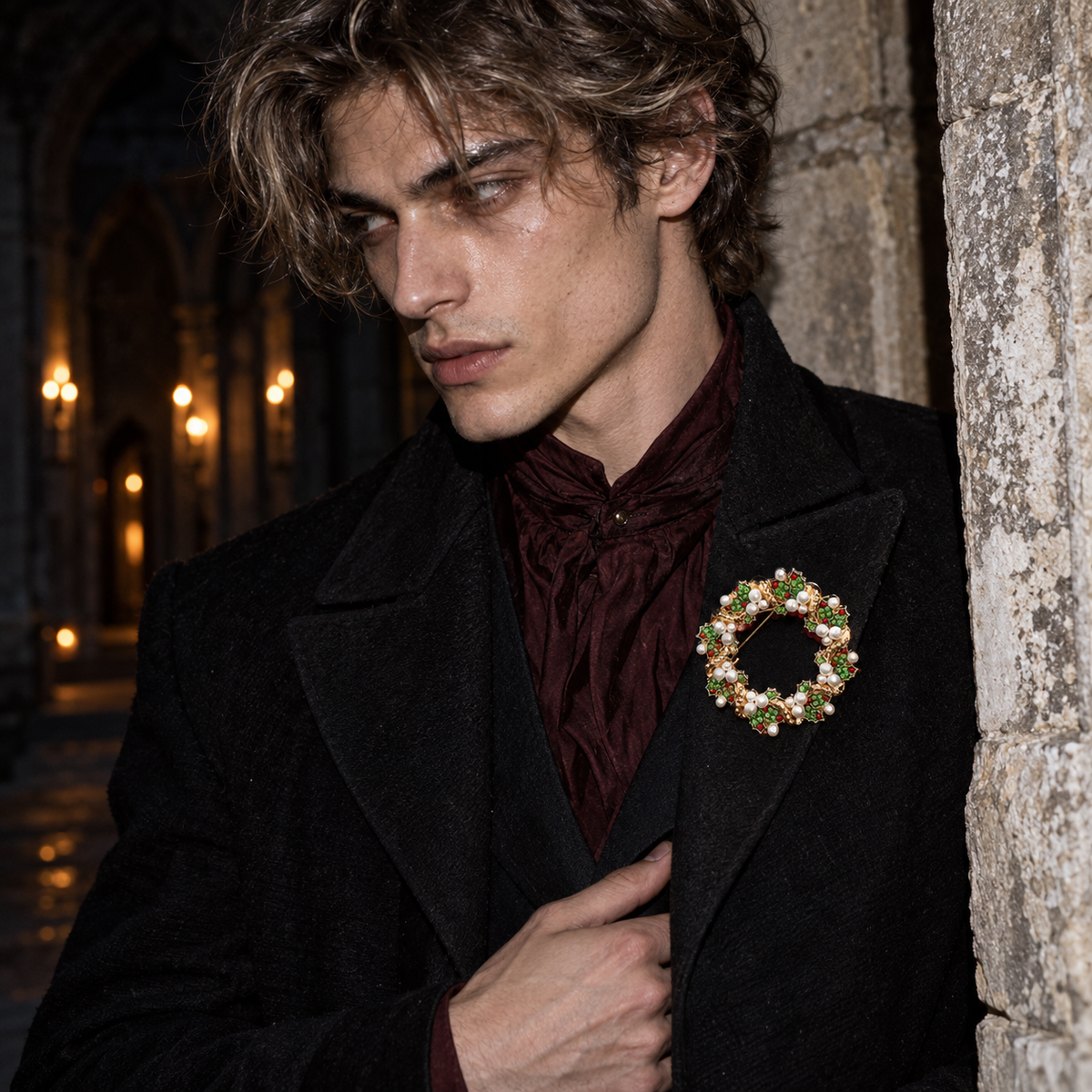 A man in a black coat and burgundy cravat wears a decorative gold-toned brooch with green leaves and white flowers, posed against a stone wall in a dimly lit interior.