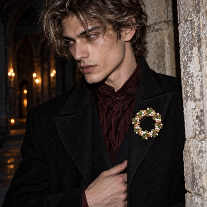 A man in a black coat and burgundy cravat wears a decorative gold-toned brooch with green leaves and white flowers, posed against a stone wall in a dimly lit interior.