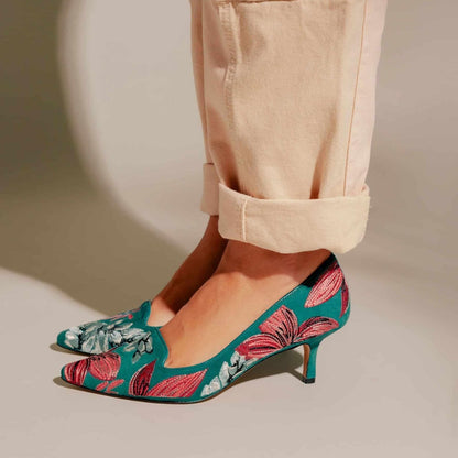 Teal kitten heels with pink floral pattern worn with beige pants on a neutral background